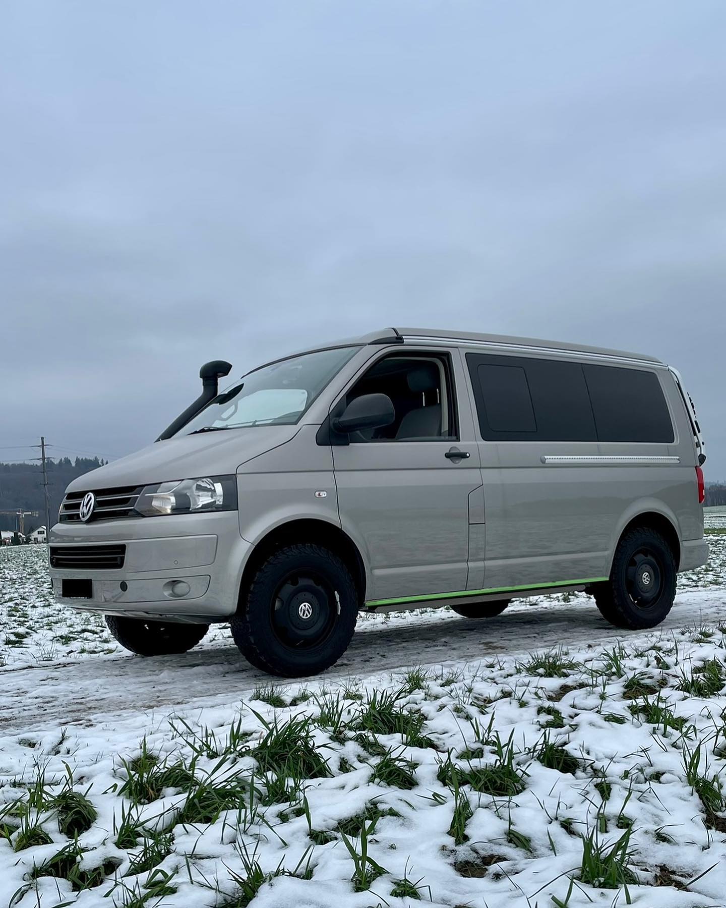 Silberner VW-Bus mit getönten Fenstern auf verschneitem Feldweg.