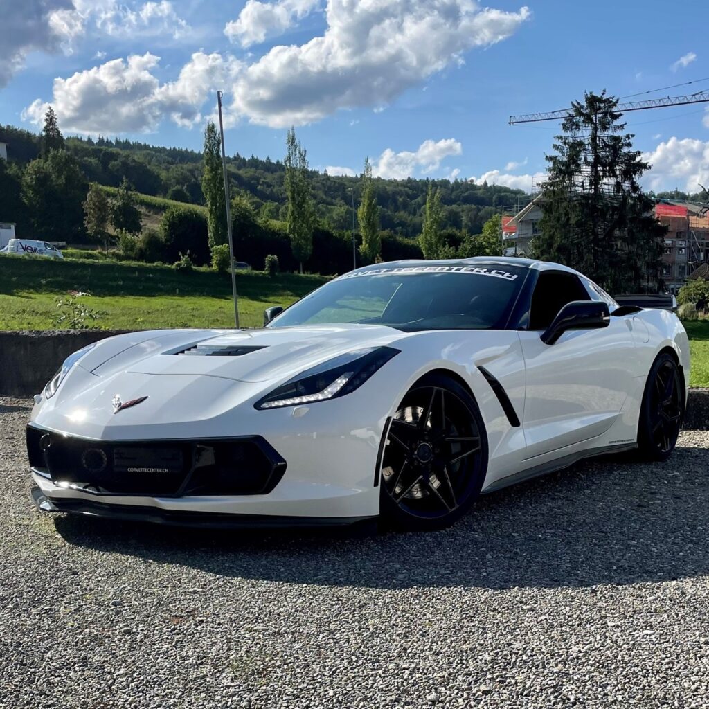 Weiße Corvette mit glänzendem Lackschutz auf Kiesplatz vor blauem Himmel.